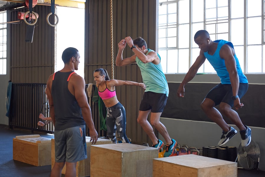A CrossFit coach oversees a group of trainees performing the box jump.