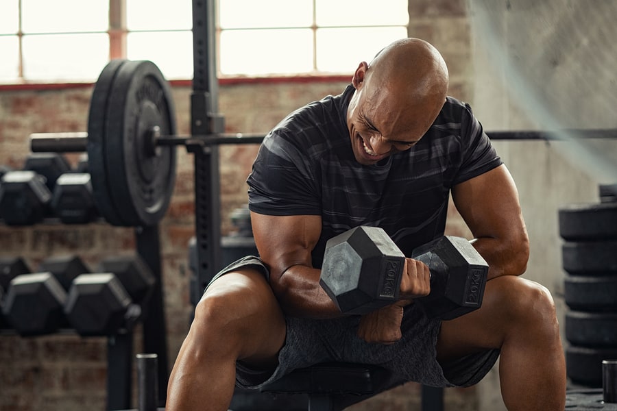 Man strength training in the gym with dumbbells.